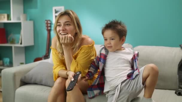 Happy child is watching cartoons on TV with loving mother at home on sofa - Imágenes, Vídeo