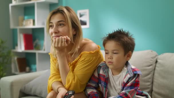 Mom and son watching TV while sitting on a couch in the living room - Filmmaterial, Video