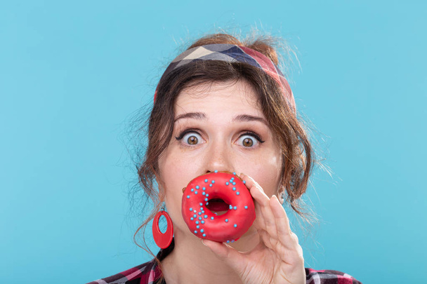 Junk food, diet and unhealthy lifestyle concept - pin-up woman closed her mouth by doughnut - Photo, Image