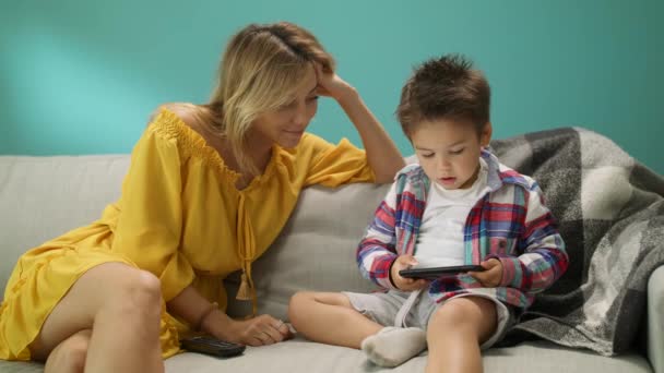 Little boy with mom plays a game on a smartphone on the couch in the living room - Кадри, відео