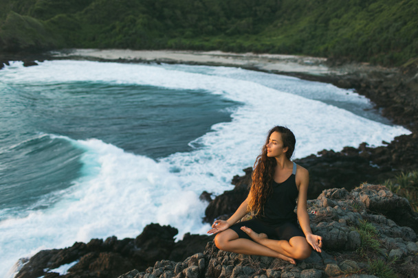 Fiatal nő gyakorló jóga lótusz pózol naplementekor a gyönyörű - Fotó, kép