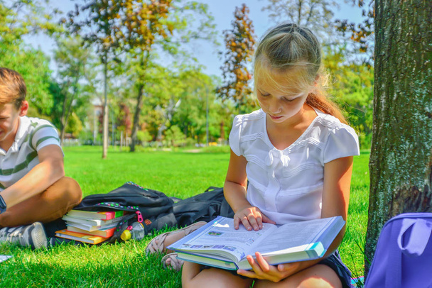I bambini fanno i compiti nel parco, un ragazzo e una ragazza si preparano per la scuola.
. - Foto, immagini