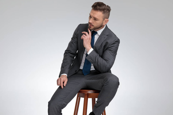 pensive young businessman sitting on stool and wonders  - Φωτογραφία, εικόνα