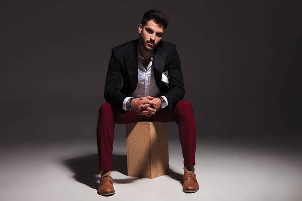 sexy elegant man sitting on box and holding hands together - Foto, afbeelding