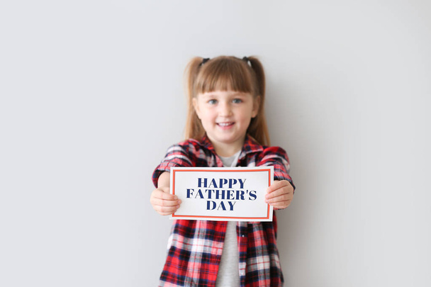 Cute little girl with greeting card for Father's Day on light background - Foto, Bild