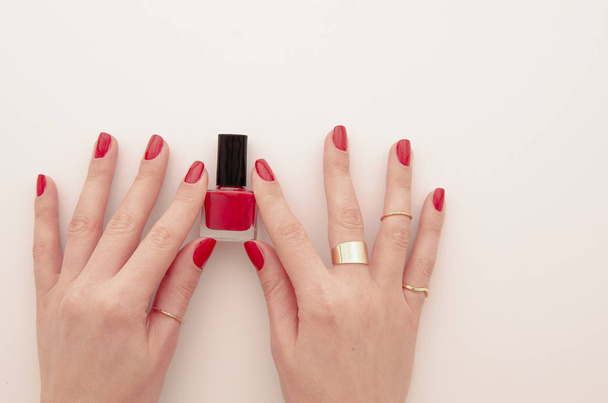 Flat lay groomed womans hands with red nail varnish bottle isolated on white. Nail varnishing in red color. Manicure concept - Photo, Image