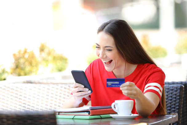 Excited student in red buying online in a bar - Photo, Image
