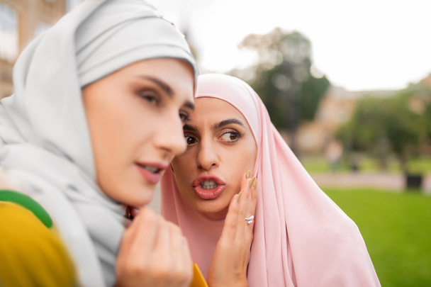 Dark-eyed muslim woman telling secret information to friend - Zdjęcie, obraz