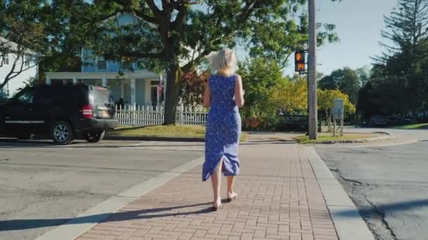 The woman crosses the road on a pedestrian crossing to the permissive signal of a traffic light. A small typical American town - Záběry, video