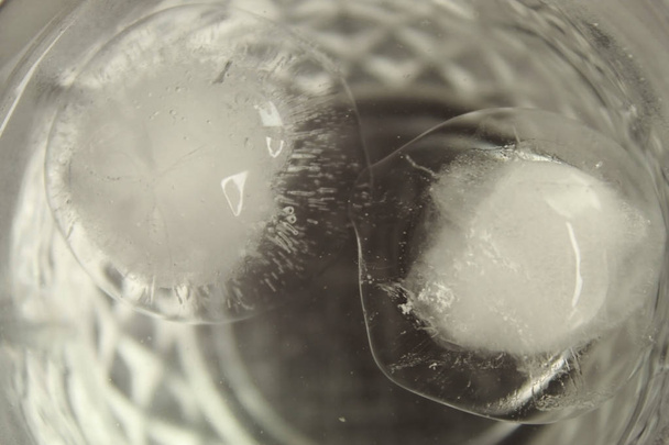 Close-up shot van ronde-vormige ijsblokjes smelten in een transparant glas water - Foto, afbeelding