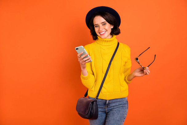 Photo of cheerful nice toothily smiling girl posing in front of camera with phone in hand while isolated with orange background - Photo, image