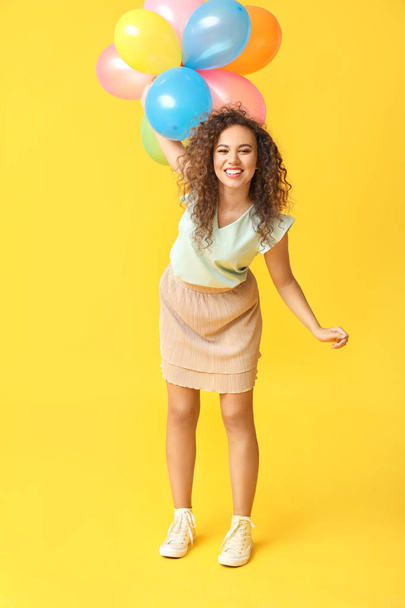 Happy African-American woman with air balloons on color background - Fotó, kép