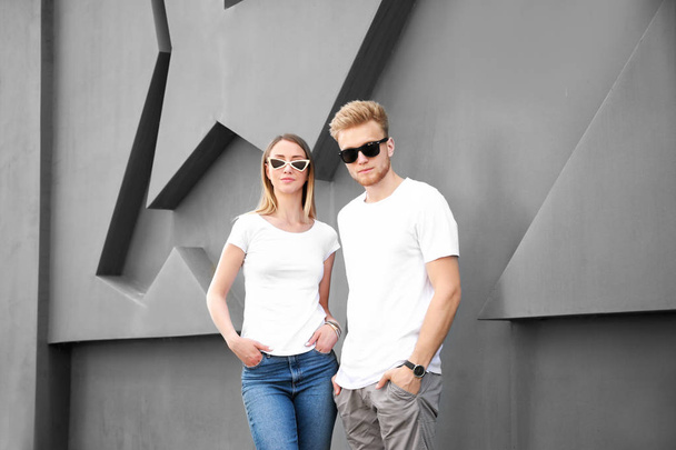 Чоловік і жінка в стильних футболках біля сірої стіни
 - Фото, зображення