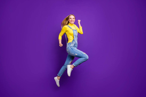 Full size photo of cheerful girl raising her fists screaming yeah wearing yellow turtleneck denim jeans isolated over purple violet background - Photo, image