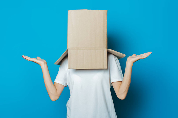 Young woman with a cardboard box on her head on a blue background - Foto, Imagem