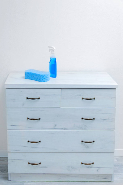 Nagy szivacs és tisztító spray egy szürke fiókos szekrény ellen, fehér falon. Az apartman takarítása. - Fotó, kép