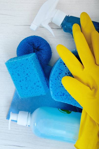 Esponjas, trapos, guantes, detergentes sobre una mesa gris sobre el fondo de una pared blanca
. - Foto, Imagen