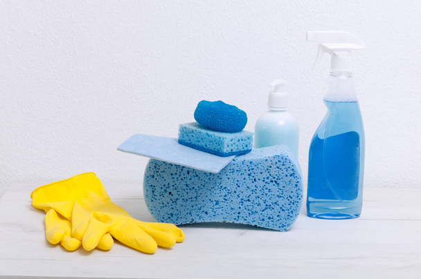 Sponges, rags, gloves, detergents on a gray table against the background of a white wall. - Photo, image