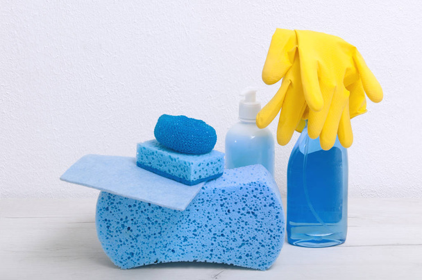 Sponges, rags, gloves, detergents on a gray table against the background of a white wall. - Foto, afbeelding