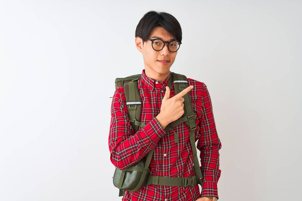 Chinese hiker man wearing backpack canteen glasses over isolated white background cheerful with a smile of face pointing with hand and finger up to the side with happy and natural expression on face - Photo, image