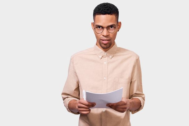 Horizontal studio portrait of serious African American young businessman in casual shirt analyzing financial reports posing in studio. Afro Male entrepreneur checking paper accounting documents. - Fotoğraf, Görsel