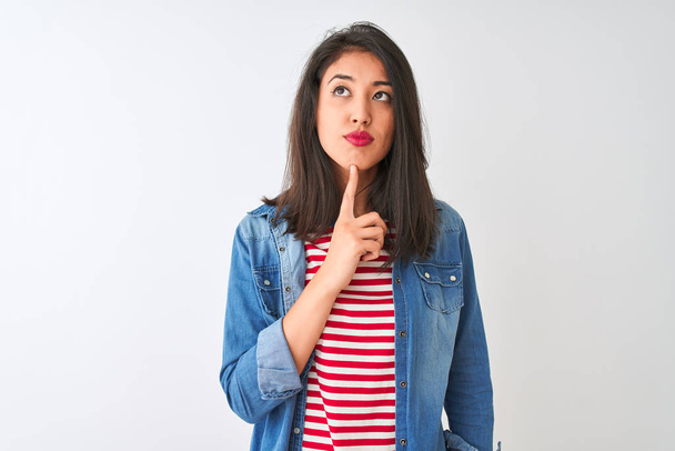 Young chinese woman wearing striped t-shirt and denim shirt over isolated white background Thinking concentrated about doubt with finger on chin and looking up wondering - Photo, Image
