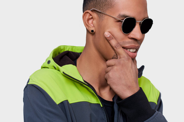 Closeup studio image of African American man posing for advertisement wears trendy black sunglasses, touching his face, isolated on white background. People, emotion and lifestyle concept - Foto, Bild