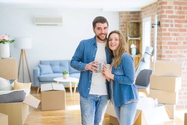 Young couple relaxing from moving to a new house drinking a coffee around cardboard boxes - Photo, Image
