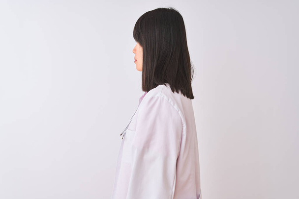 Genç güzel Çinli doktor kadın izole beyaz arka plan üzerinde stetoskop giyen yan bakarak, kendine güvenen gülümseme ile doğal yüz ile profil poz dinlenmek. - Fotoğraf, Görsel
