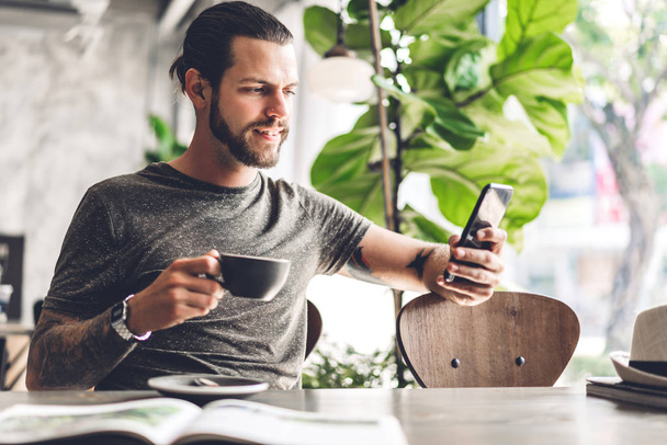 schöner bärtiger Hipster-Mann nutzt Smartphone mit Kaffee am Tisch - Foto, Bild