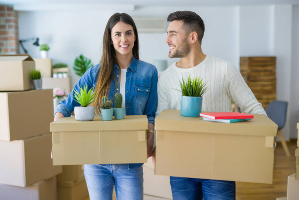 Молодая пара переезжает в новый дом, улыбаясь счастливо держа картонные коробки в новой квартире
 - Фото, изображение