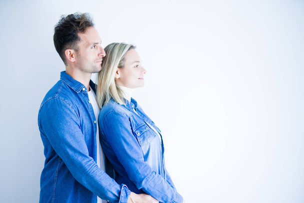 Молодая красивая пара в джинсовой рубашке стоя на изолированном белом фоне глядя в сторону, расслабиться профиль позировать с естественным лицом с уверенной улыбкой
. - Фото, изображение