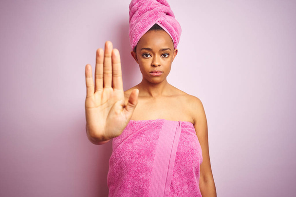 Mujer afroamericana con toalla de ducha después del baño sobre fondo rosa aislado haciendo dejar de cantar con la palma de la mano. Expresión de advertencia con gesto negativo y serio en la cara
. - Foto, Imagen