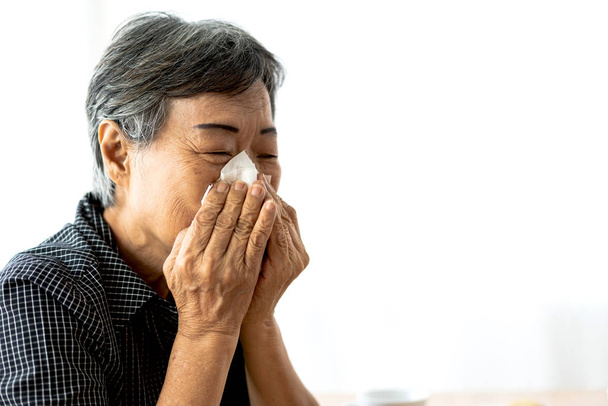 Άρρωστη ηλικιωμένη γυναίκα που ανατινάζει τη μύτη της με χάρτινο ιστό και το σνίν - Φωτογραφία, εικόνα