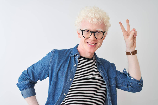 Fiatal albínó szőke ember visel farmer inget és poharat át elszigetelt fehér háttér mosolyog szeretnének a kamera mutatja ujjak csinál győzelem jele. Kettes számú. - Fotó, kép