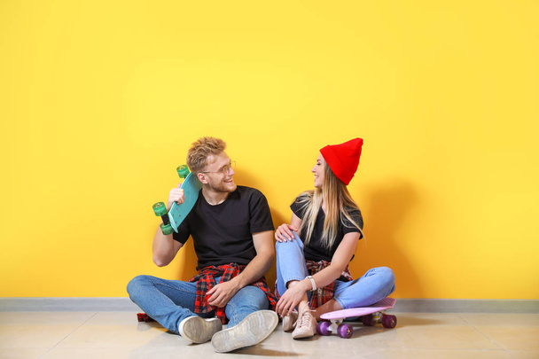 Couple in stylish t-shirts and with skateboards sitting near color wall - Foto, imagen