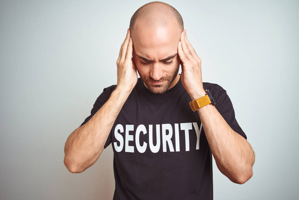 Young safeguard man wearing security uniform over isolated background with hand on head for pain in head because stress. Suffering migraine. - Foto, imagen