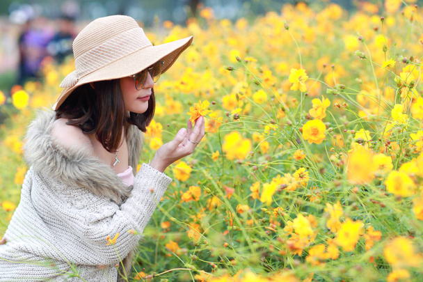 cute and beautiful girl with hat standing in nature outdoors among cosmos flowers field (rest time on vacation concept) - Photo, Image