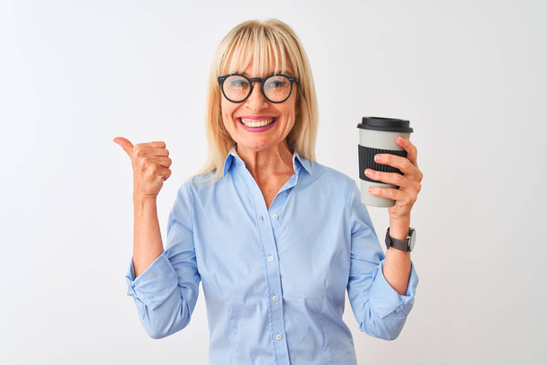Middle age businesswoman wearing glasses drinking coffee over isolated white background pointing and showing with thumb up to the side with happy face smiling - Foto, afbeelding