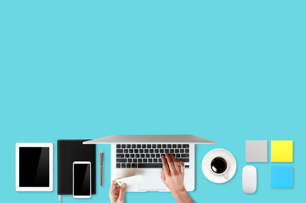 mesa de trabajo de la tecnología con las manos de la mujer en el ordenador portátil, tarjeta de crédito, taza de café y teléfono celular sobre fondo verde (o concepto de compras y pago en línea
) - Foto, Imagen