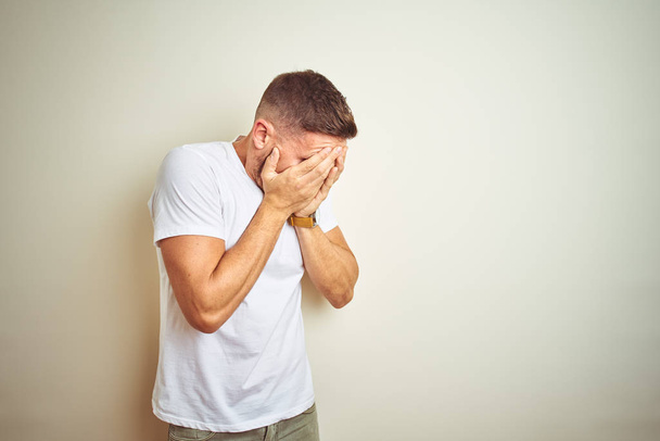 Young handsome man wearing casual white t-shirt over isolated background with sad expression covering face with hands while crying. Depression concept. - Photo, Image