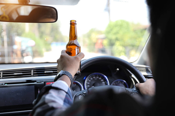 άνθρωπος οδήγηση αυτοκίνητο και κρατώντας μπουκάλι αλκοόλ σε ένα άλλο χέρι, ενώ στο δρόμο  - Φωτογραφία, εικόνα