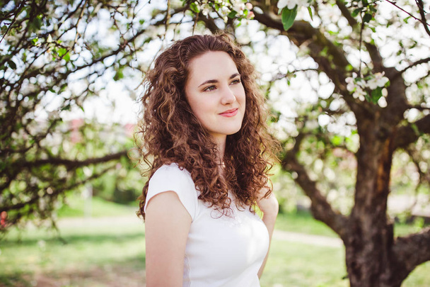 Giovane donna allegra in una t-shirt bianca sotto l'albero in fiore
. - Foto, immagini