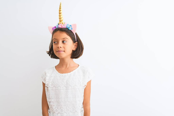 Beautiful child girl wearing unicorn diadem standing over isolated white background smiling looking to the side and staring away thinking. - Foto, Imagem