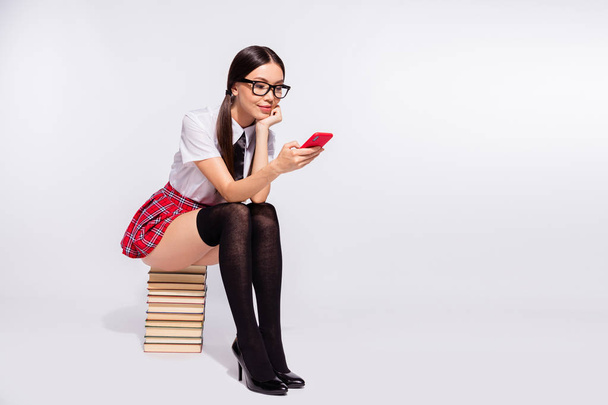 Full length body size photo beautiful she her teacher sit book pile spend lesson time internet boredom texting telephone wear specs red checkered costume pantyhose tights isolated white background - Foto, immagini