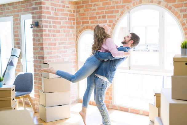 Young beautiful couple in love celebrating moving to a new home around cardboard boxes - Photo, image