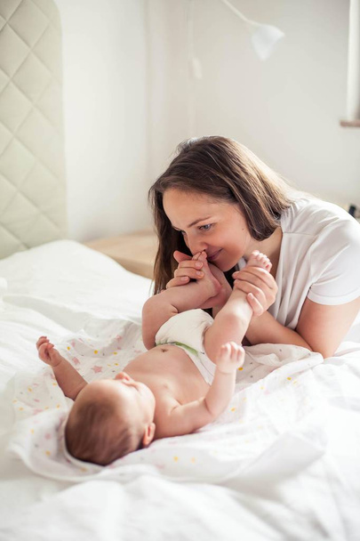 Young beautiful mother holds a baby. Mom kisses her baby. Childrens bedroom. - Photo, Image