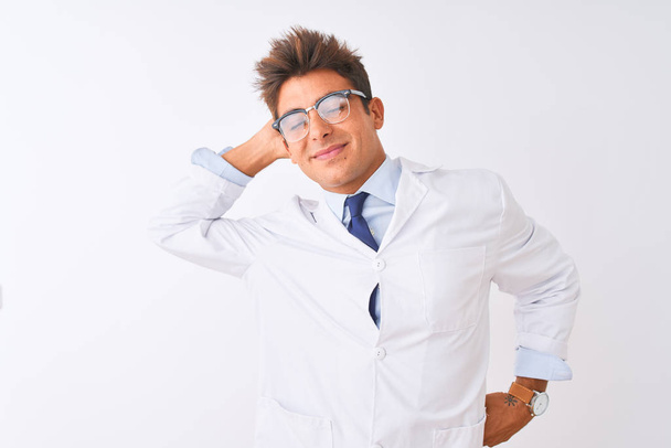 Jonge knappe sciencist man het dragen van een bril en jas over geïsoleerde witte achtergrond stretching terug, moe en ontspannen, slaperig en geeuwen voor de vroege ochtend - Foto, afbeelding