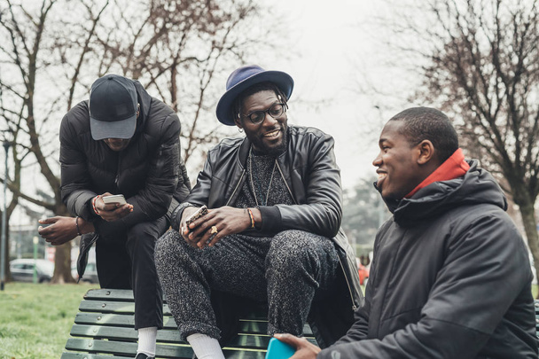Üç Afrikalı arkadaş dışarıda oturuyor ve akıllı telefonlara bakıyor. - Fotoğraf, Görsel