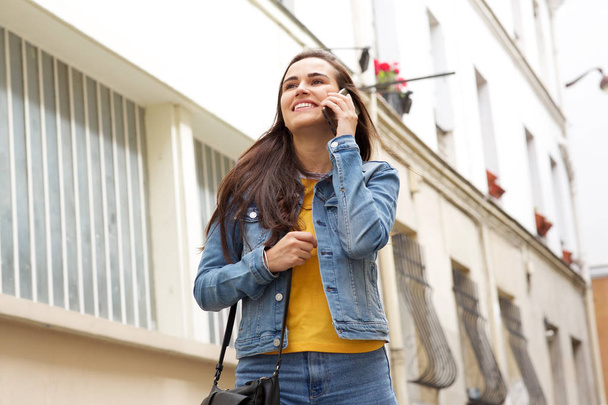 Porträt einer glücklichen jungen Frau, die durch die Stadt geht und mit dem Handy spricht - Foto, Bild